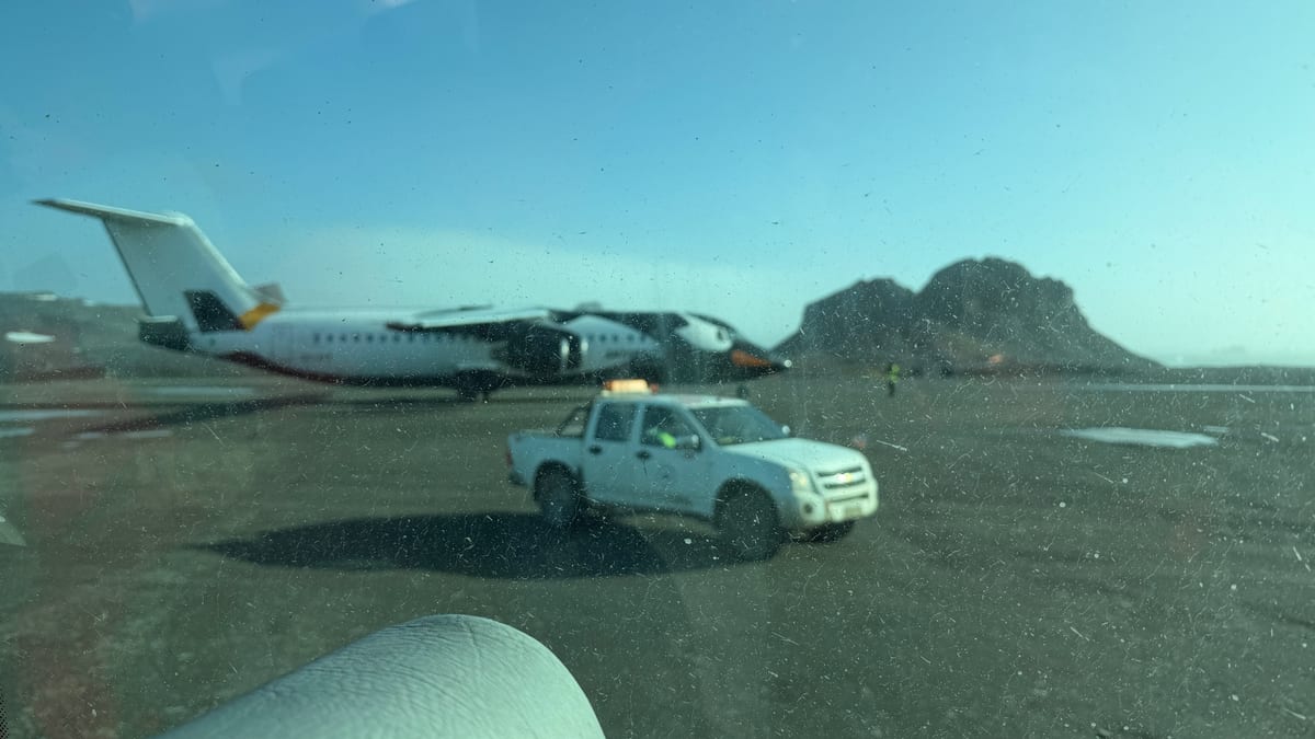 隔著窗戶看出去的喬治王島機場，地面是碎石，遠處停著一架包機